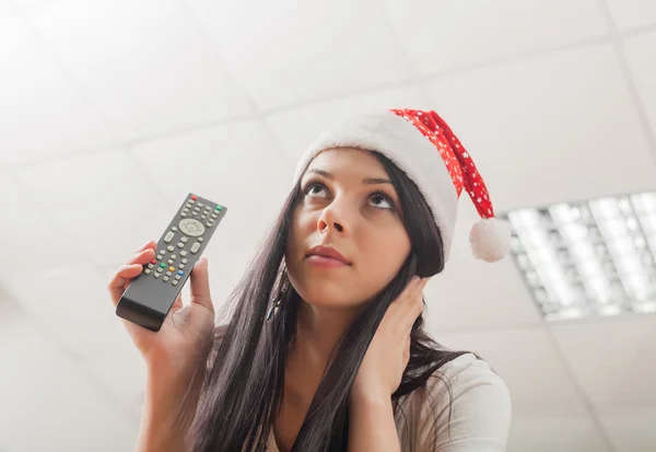 黑发女子穿着圣诞老人的帽子与远程控制在手里 — 图库照片