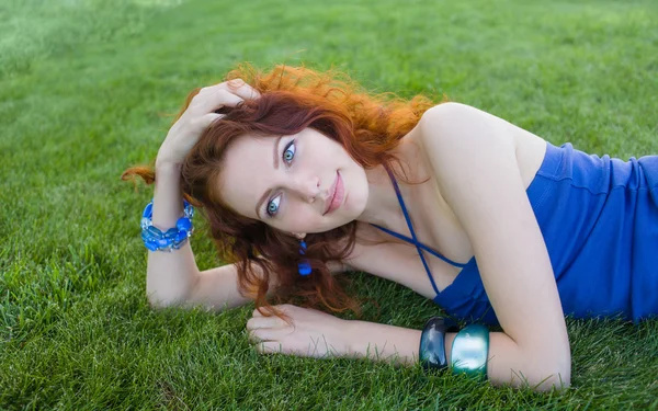 Красивая рыжая девушка лежит на зеленой траве — стоковое фото