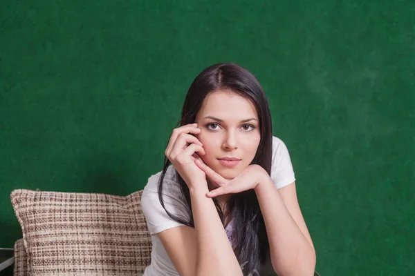 Brunette indoors sitting against green wall — Stock Photo, Image