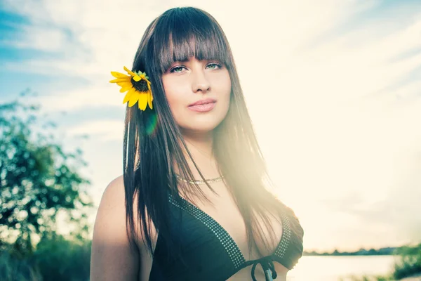 Pretty woman against sky with sunflower in her hair — Stock Photo, Image