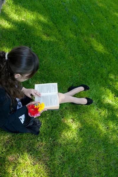 Brunetka kobiet czytanie, siedząc na zielonej trawie w parku miejskim — Zdjęcie stockowe
