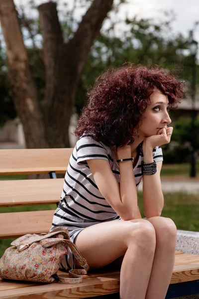 Una hermosa chica está sentada en un banco del parque —  Fotos de Stock