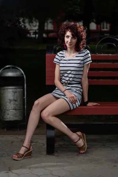 Une belle fille est assise sur un banc de parc — Photo