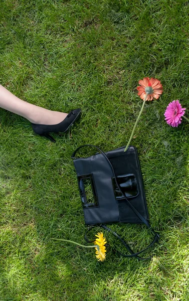 Jambes, sac à main et fleurs sur herbe — Photo