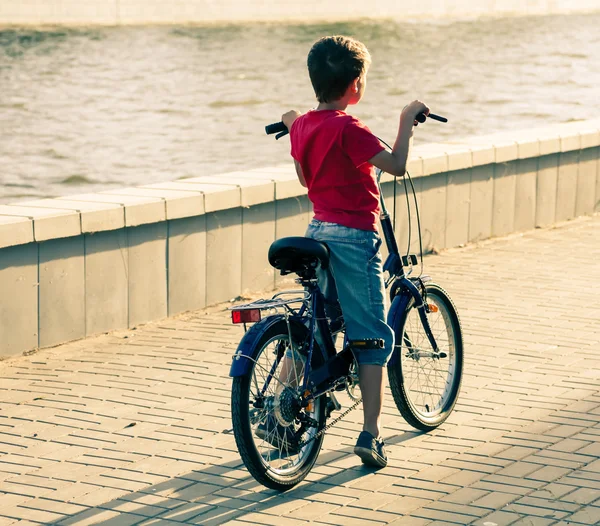 背面观的一个男孩骑自行车靠近水的地方 — 图库照片