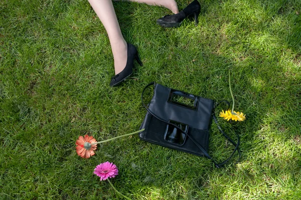 Pernas, bolsa e flores na grama — Fotografia de Stock