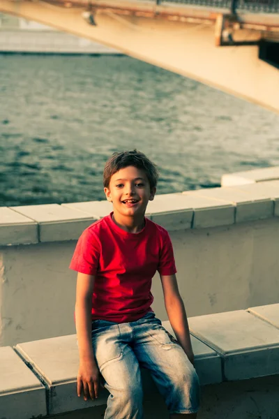 Мальчик сидит на парапете возле пруда — стоковое фото