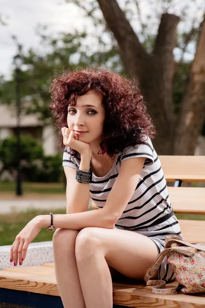 Une belle fille est assise sur un banc de parc — Photo