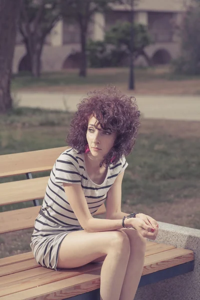 A beautiful girl is sitting on a park bench — Stock Photo, Image