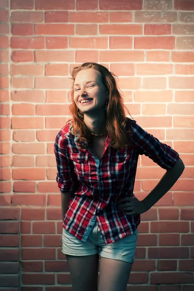 Femme rousse souriant contre le mur de briques rouges — Photo