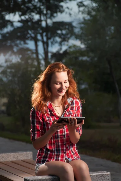 Ginger haired woman sitting on park bench and uding tablet-pc — Stock Photo, Image