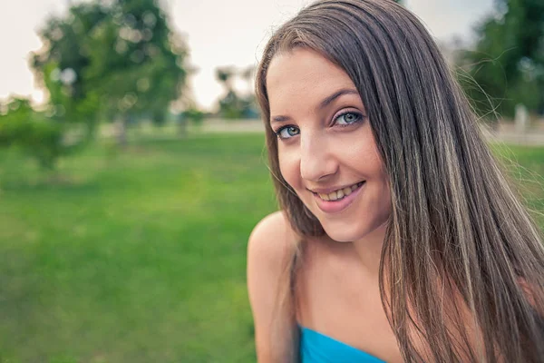 这位年轻的微笑的女士 留着一头长长的金发 在公园里摆姿势 带着色彩 — 图库照片