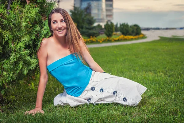 かわいい魅力的な若い女性の写真長いブロンドの髪は地面にもたれて緑の草の上に休んで青いオフショルダーシャツを身に着けている — ストック写真