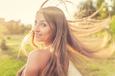 Neşeli bayan uzun sarı saçlarıyla geriye bakıyor havada uçuyor ve ılık yaz güneşiyle aydınlanıyor..