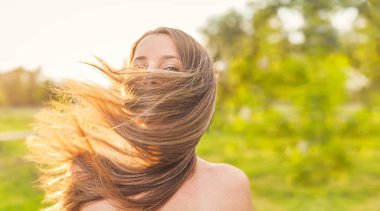 Uzun sarı saçlarına sarılı mutlu kadın yüzü rüzgarın esintisi, neşesizlik ve özgür yaz manzarası..