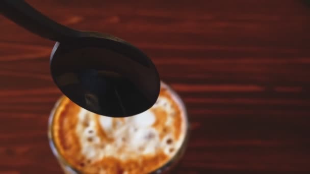 POV of spoon moving down into flat-white coffee in slow motion, from out-of-focus to in-focus closeup — Stock Video