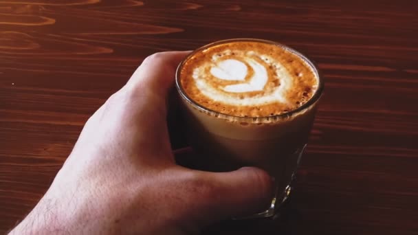 Horní pohled na šálek kávy ploché bílé s krásnou latte pěny umění na vrcholu na dřevěném stole, které drží pánské ruce — Stock video