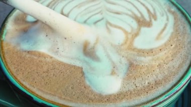 Köpüklü üst yüzeyin çok yakından çekilmiş fotoğrafı. Sıvıdan latte sanatı ve kaşık geliyor.