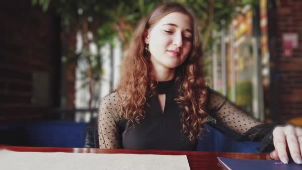 Сором'язлива дівчина з довгим коричневим волоссям сидить у кафетерії і добре посміхається, дівчинафранцузькі знайомства — стокове відео