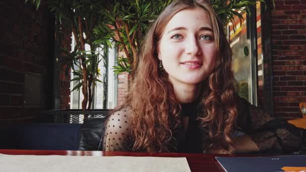 Trevlig flicka med långt brunt hår sitter i cafeterian och pratar med sin visavis, slomo — Stockvideo