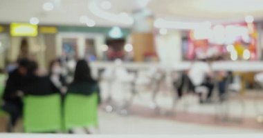 Birçok insan büyük bir alışveriş merkezinde yemek yiyor. Arka plandaki zaman dilimi olarak masalarda oturuyor.