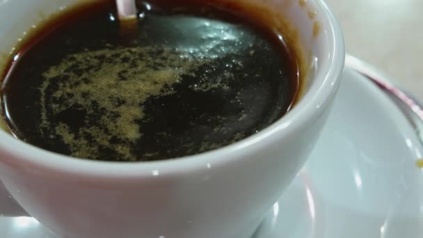 Mischen von schwarzem Kaffee mit metallischem Löffel in weißer Keramiktasse auf silbernem Tisch — Stockvideo