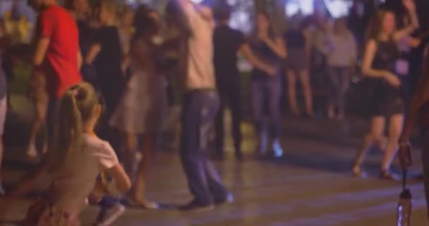 Wiele par tańczy latynoamerykańskie tańce na zewnątrz, mała dziewczynka próbuje wykonać te same ruchy taneczne na pierwszym planie. Uliczny taniec salsy w nocy, wiele młodych par tańczy towarzyskie tańce latynoskie — Wideo stockowe