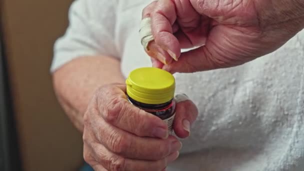 Starší žena odstraňuje těsnící kroužek kolem plastového uzávěru na lahvičce s pilulkami — Stock video