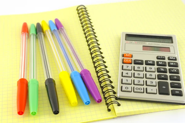 Old calculator and color pens on the yellow writing-book — Stock Photo, Image