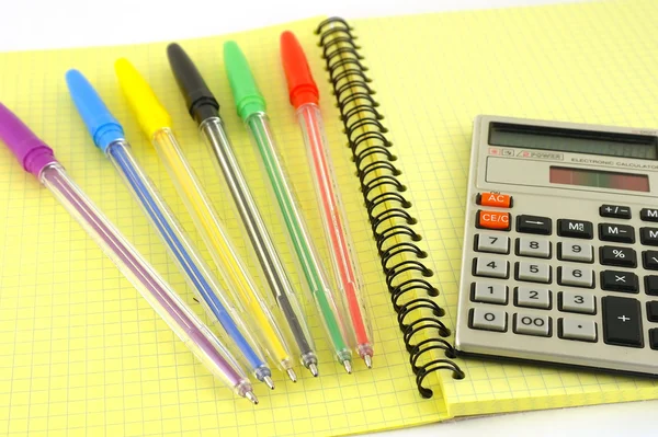 Old calculator and color pens on the yellow writing-book — Stock Photo, Image