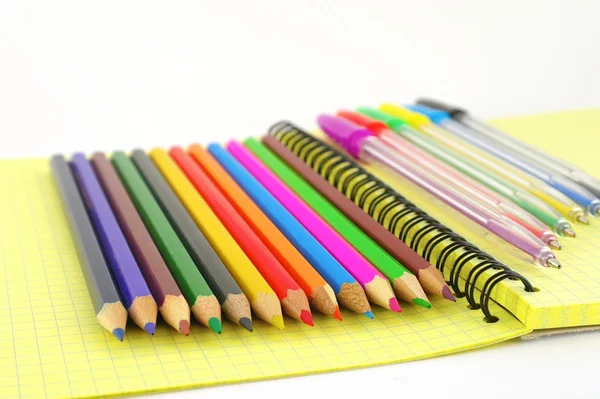 Color pen and pencils on the yellow writing-book — Stock Photo, Image