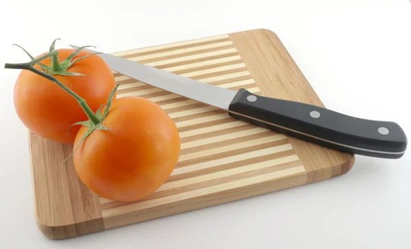 Faca de cozinha e tomates vermelhos na placa de preparação — Fotografia de Stock