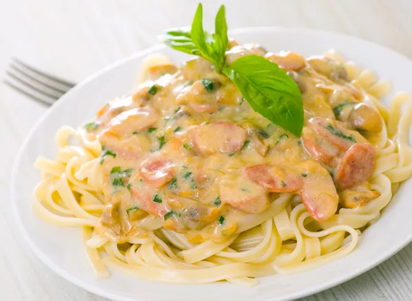 Nudeln mit Pilzen, geräucherter Wurst und Sahnesoße mit Basilikum — Stockfoto