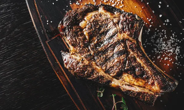 Grilled Ribeye Steak on bones on wooden board, prime cowboy steak on dark background