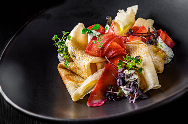 Crepes with smoked gravlax salmon on black plate on wooden table dark background