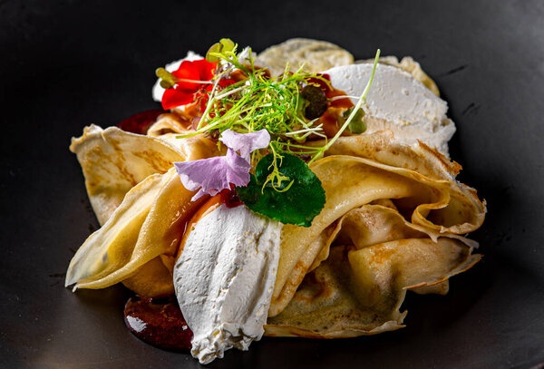 Crepes with strawberries jam and cream cheese on black plate on wooden table dark background