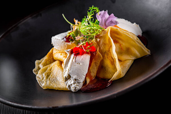 Crepes with strawberries jam and cream cheese on black plate on wooden table dark background