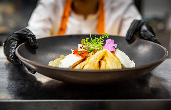Chef's hands in gloves cooking crepe pancake on plate in kitchen