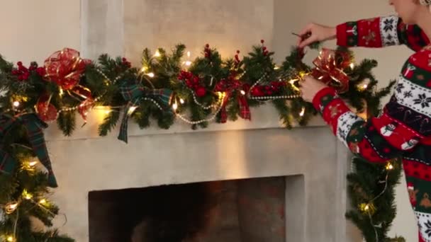 Mujer está decorando la chimenea de Navidad en suéter con un patrón de Navidad — Vídeos de Stock