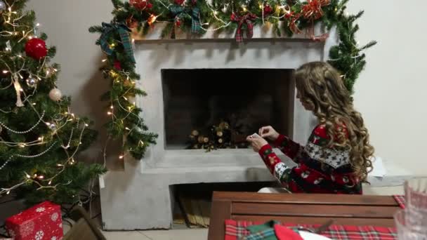 A young woman in sweater with a Christmas pattern lights a fireplace — Stock Video