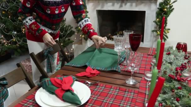 Молодая женщина в свитере с рождественским рисунком украсила новогодний стол — стоковое видео