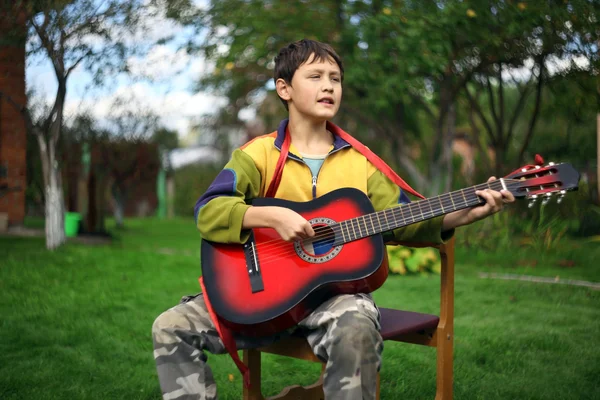 Jongen speelt de gitaar en het zingen buitenshuis — Stockfoto