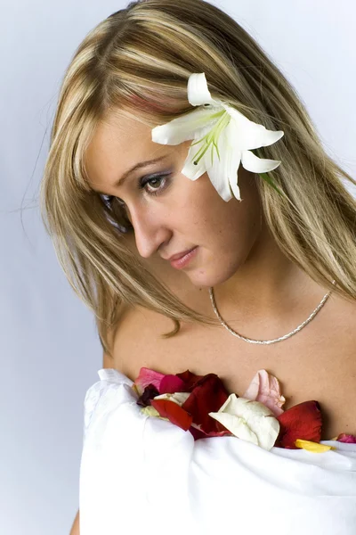 Cute blondie with naked shoulders laying covered with rose petals and lily — Stock Photo, Image