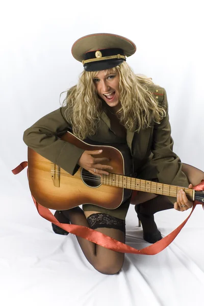 Blondine in alter sowjetischer Militärform und schwarzen Strümpfen posiert im Studio mit traditioneller russischer Akustikgitarre — Stockfoto