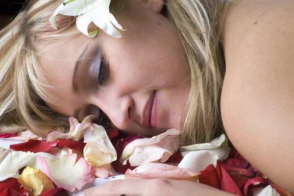 Süße Blondine mit nackten Schultern, die mit Rosenblättern bedeckt liegt — Stockfoto