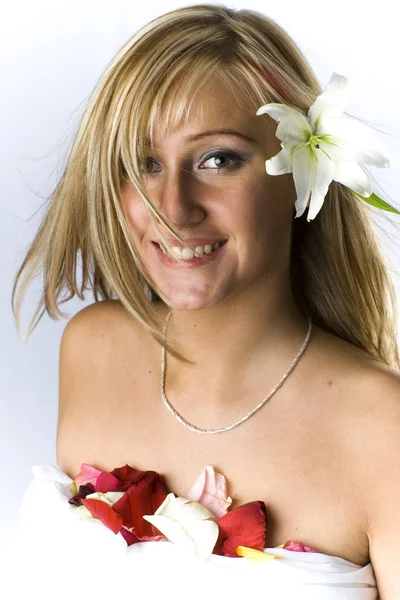 Cute blondie with naked shoulders laying covered with rose petals and lily — Stock Photo, Image