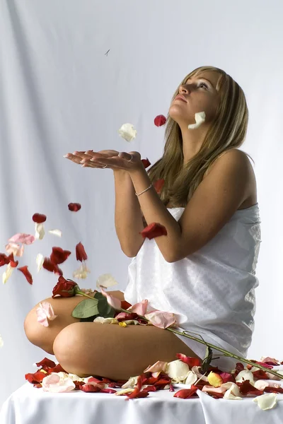 Süße Blondine mit nackten Schultern, die mit Rosenblättern bedeckt liegt — Stockfoto