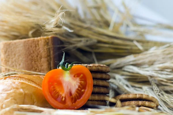 Wheat ears, Fresh red tomato, cookies and bread bagels on wooden table — Stock Photo, Image