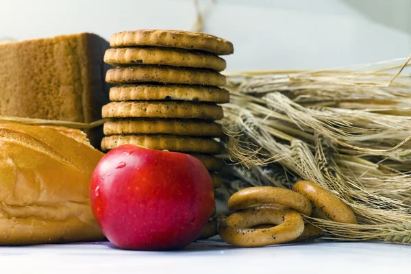 Wheat ears, Fresh red apple, cookies and bread bagels on wooden table — Stock Photo, Image