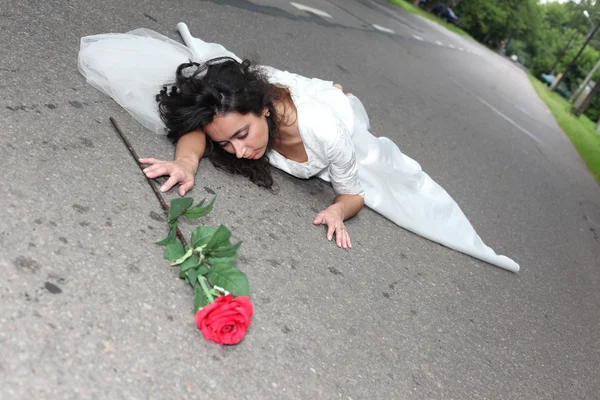 Noiva com rosa deitada em uma estrada — Fotografia de Stock